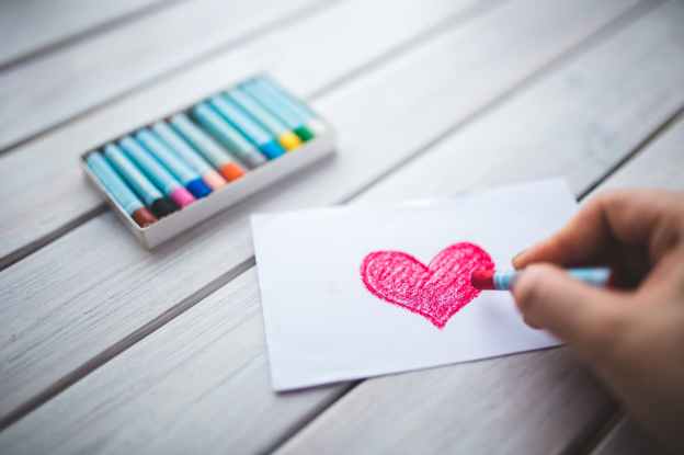 hand with oil pastel draws the heart